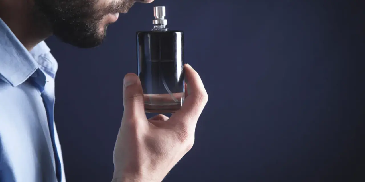 Mężczyzna wącha perfumy z buteleczki.