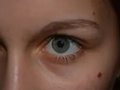 Zbliżenie na zielone oko z pieprzykiem, przypominającym znamie Spitza, na policzku.