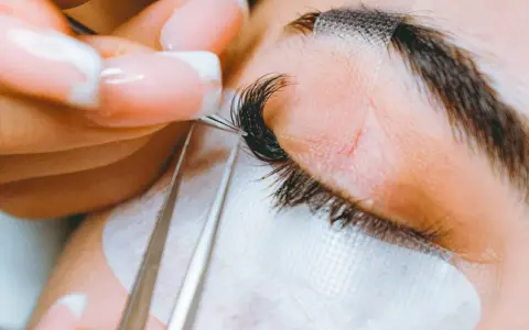 Precyzyjne przedłużanie rzęs: porównanie rzęsy 2d i 3d. Stylistka z perfekcyjnym manicurem dokłada kępki.