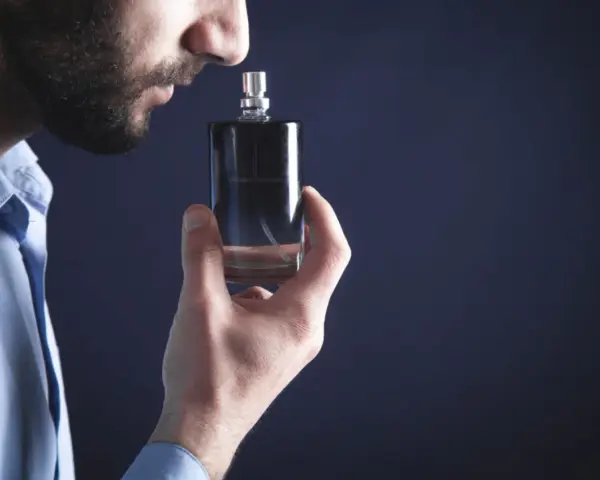 Mężczyzna wącha perfumy z buteleczki.