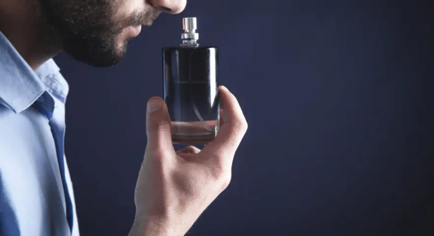 Mężczyzna wącha perfumy z buteleczki.